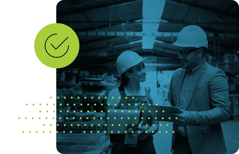 Two workers in hard hats look at a tablet in an industrial setting.