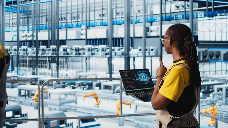 Female engineer using laptop to manage operations in smart factory